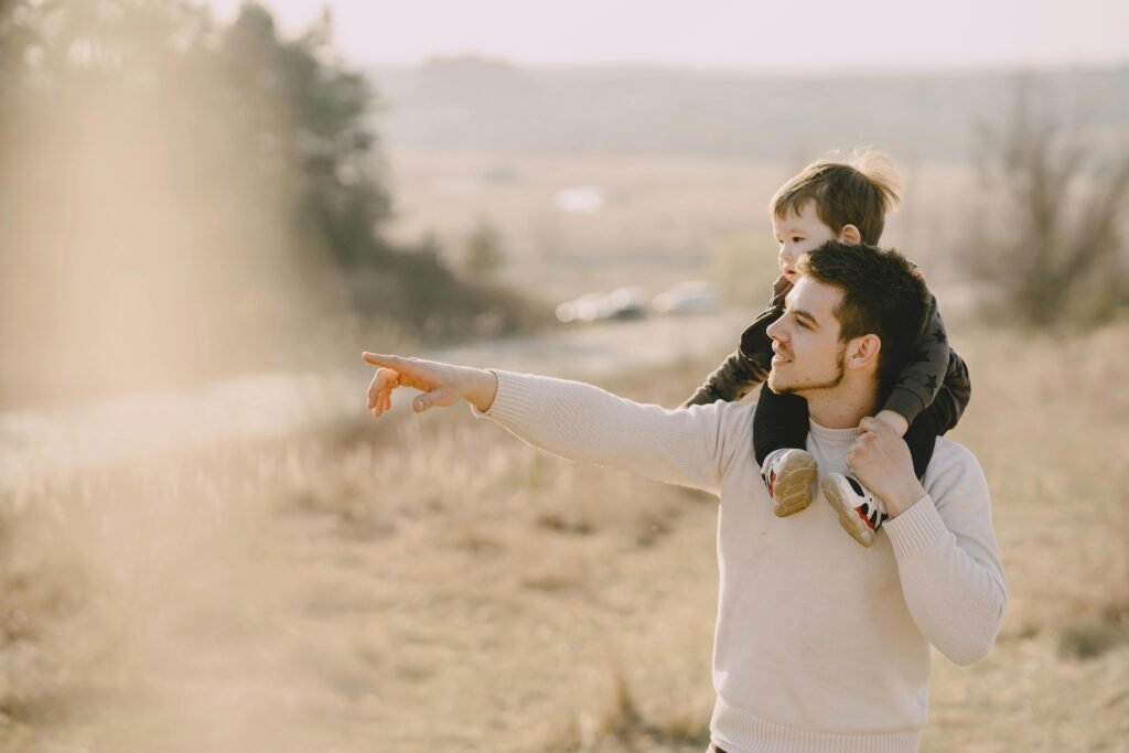 pexels photo 4148850 4148850 A father carries his child on his shoulders, pointing towards the horizon on a sunny day outdoors.