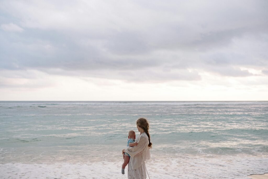 A serene beach scene featuring a mother holding her baby by the ocean during summer.