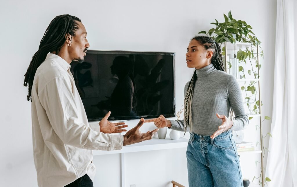 Side view of nervous young African American man and woman with dreadlocks in casual clothes quarreling together in light living room